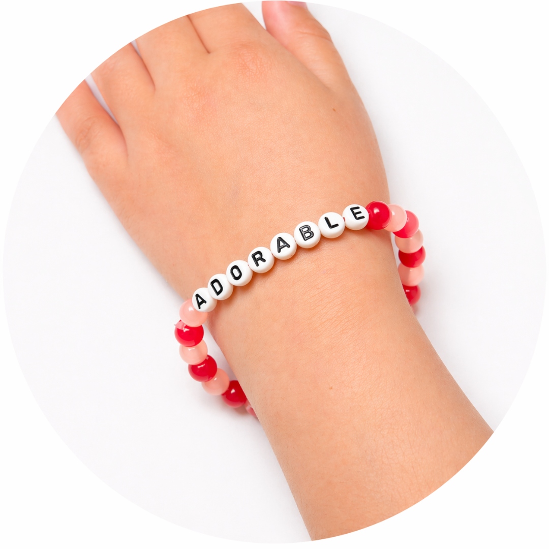 A pink-and-red beaded stretchy bracelet spelling ADORABLE on a child's wrist.
